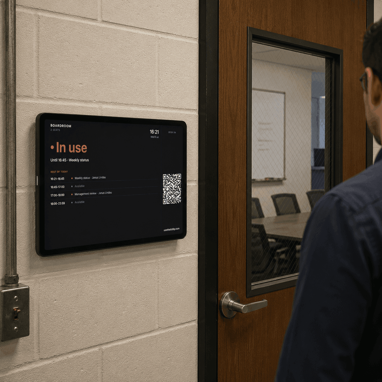 A tablet mounted beside a meeting room showing the live room view